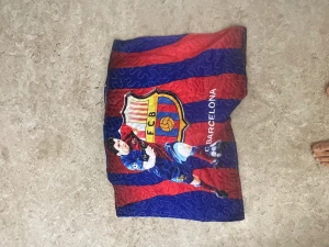 FC Barcelona quiltad väst - Säljer en quiltad väst med FC Barcelona-tryck i rött och blått, med klubbens emblem och en fotbollsspelare på framsidan. Västen har breda ränder och är tillverkad i syntetmaterial, perfekt för dig som älskar fotboll och vill sticka ut med din stil.