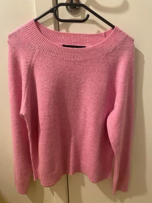 Rosa stickad tröja från Vero Moda - Mysig rosa stickad tröja från Vero Moda med bred ribbad halsringning och långa ärmar. Perfekt för att addera lite färg till din garderob. Tröjan har en enkel och clean design med ribbade muddar vid ärmslut och nederkant. Har använt 1 gång 