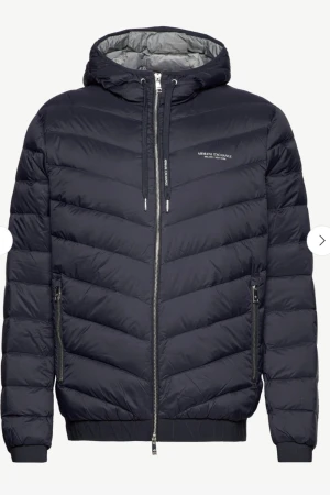 Mörkblå Armani Exchange DOWN JACKET  - Snygg mörkblå pufferjacka från Armani Exchange med huva och dragkedja framtill. Jackan har quiltad design i chevronmönster, ribbade muddar och två sidofickor med dragkedja. Perfekt för kalla dagar och har en clean, modern look. Garanti endast haft den 1 gång. Storlek M.