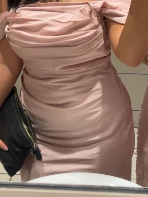 Ljusrosa  långklänning - Elegant ljusrosa långklänning i glansigt material med draperad överdel och axelbandslös design. Klänningen har figurnära passform och slät kjol som faller snyggt längs kroppen. Perfekt för speciella tillfällen när du vill sticka ut.  Axel band finns på men kan tas bort om det önskas. Banden är själv påsytt. Använd 2 gånger 