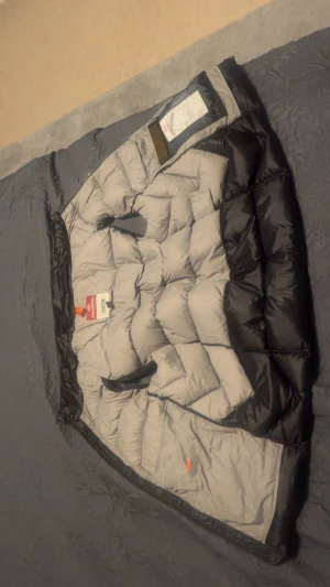 Svart dunväst med dragkedja - Säljer en svart dunväst från Sheen med quiltad design och dragkedja framtill. Västen har en hög krage med gul detalj och är perfekt att slänga över en hoodie. Passformen är normal och materialet är polyester med dunfyllning.