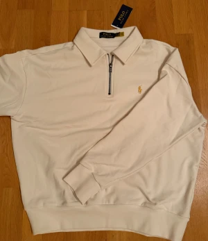 Pikétröja Ralph Lauren Oversized - Oanvänd vit pikétröja från Polo Ralph Lauren med klassisk krage och half zip framtill. Tröjan är oversized och passar den som bär M/L i storlek. 