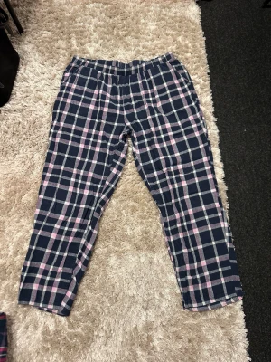 Rutig mjukisbyxa från Esmara XL - Mysiga mjukisbyxor från Esmara i storlek XL med ett snyggt rutigt mönster i mörkblått, rosa och vitt. Byxorna har elastisk midja och är perfekta för chill hemma. Materialet är mjukt och skönt mot huden.