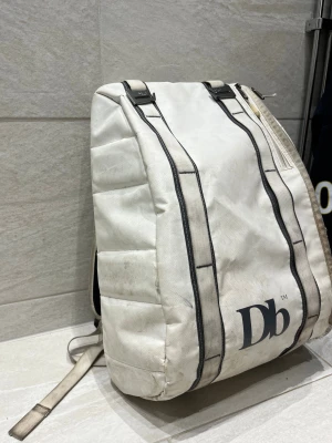 Douche bag 15L hugger base - Säljer min DB väska då den inte används. Finns tecken på slitage, se bilderna. Den är väl använd men fortfarande funktionell. Den vita färgen gör den till en fräsch ryggsäck. Det är en äldre modell som är flera år gammal.  Volym: 15L  Hör av dig om du har frågor eller vill ha fler bilder:)