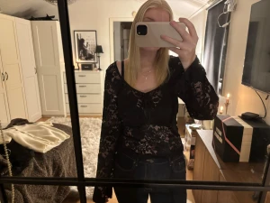 Svart spetsblus från Pieces - Svart blus från Pieces i storlek M, med genombruten spets och blommigt mönster. Blusen har långa ärmar, v-ringning och en söt knytning framtill🖤