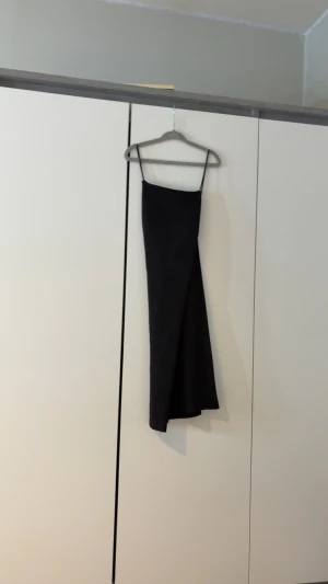 Svart ribbad klänning H&M Divided S - Svart ribbad kortklänning från H&M Divided i storlek S. Klänningen har smala axelband och en stilren, figurnära passform med omlott-detalj framtill. Perfekt för dig som gillar minimalistisk och trendig stil.