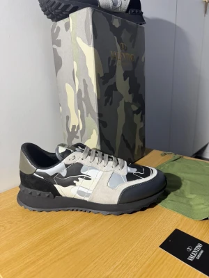 Valentino Rockrunner - Snygga Valentino Garavani Rockrunner sneakers med svart, grått och vitt camouflagemönster. Skorna har detaljer i mocka och skinn, Klassisk snörning och rund tå. Kommer med originalkartong och dustbag. Skorna är i nytt skick väldigt fina. Skick 10/10 hör av er vid funderingar.