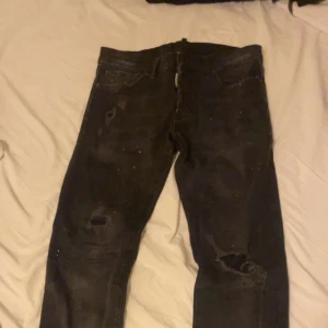 Svarta Dsquared2 slim jeans - Svarta jeans från Dsquared2 med slim passform och lätt slitna detaljer på benen. Modellen är Easy Slim Jean och har klassisk femficksdesign. Jeansen är tillverkade i Italien och har en cool, urban vibe med små färgstänk och slitningar.