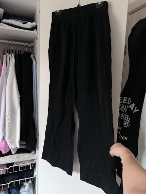Svarta byxor med resårmidja - Snygga svarta byxor med resårmidja för en bekväm passform. Byxorna har en loose stil och är perfekta för en avslappnad look. Tillverkade i ett lätt material som ger en skön känsla. Byxorna har blivit lite noppriga men borde gå bort enkelt med avnoppringsmaskin ☺️ 
