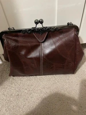 Kuvertväskor i läderlook med metallspänne - Köptes utomlands för ca 1299kr Både väskorna är likadana förutom färgen. Är aldrig används och är helt nya.                                                                     Två kuvertväskor i klassisk design, en i mörkbrunt och en i svart konstläder. Båda har dekorativa metallspännen upptill och synliga sömmar som ger en vintagekänsla. Perfekt för dig som gillar retrostil och vill ha en unik accessoar till din outfit.