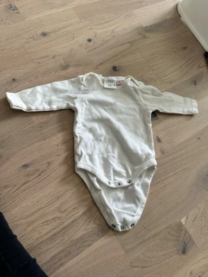 Vit långärmad body ZARA - Vit body med långa ärmar och tryckknappar nedtill. Säljer en enkel och mjuk vit långärmad body från Zara i storlek 62, Bodyn har tryckknappar i grenen för enkel påklädning och rund halsringning. Perfekt basplagg i bomull för de minsta. 