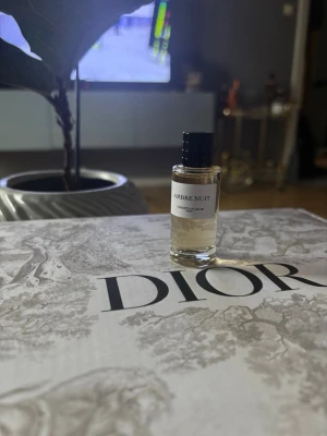 Dior Ambre Nuit parfym 10 ml (Resestorlek) - Lyxig parfym från Dior, Ambre Nuit, i en liten cylinderformad glasflaska med svart kork. Flaskan har en stilren vit etikett och kommer med en elegant vit förpackning. Doften är exklusiv och passar dig som gillar unika och sofistikerade parfymer.