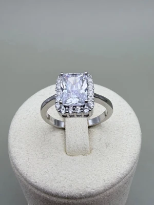 Princess-cut ring i äkta silver (925) med Zirconia  - Stilren princess-cut ring i äkta silver (stämplat 925) med en stor, rektangulär klar Zirconia i mitten, omgiven av små gnistrande stenar runt hela infattningen. Ringen har en klassisk och elegant design som verkligen drar blickarna till sig. Helt ny. Storlek: US 6/ ca. 16,5 mm i innerdiameter.