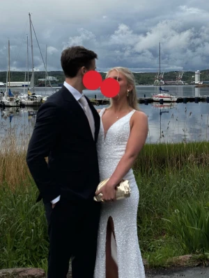 Elegant vit balklänning i paljetter, öppen rygg, stl 38 - Säljer min vackra balklänning som jag bar förra året🤍 Det är en vit, golvlång klänning täckt av glittrande paljetter som fångar ljuset. Den har en elegant V-ringning, en snygg slits framtill och en öppen rygg med justerbar snörning som gör att klänningen sitter perfekt. Ett litet släp ger en lyxig känsla.  Jag är 170 cm lång och klänningen är i storlek 38, den går ner till marken på mig. Kemtvättad efter användning. Några få paljetter saknas längst ner på släpet efter kemtvätt, syns dock knappt!