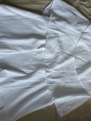 Vit kortklänning i bomull - Fräsch vit kortklänning i bomull med enkel och stilren design. Klänningen har en mjuk struktur och är perfekt för varma dagar. Passar dig som gillar klassiska och tidlösa plagg.