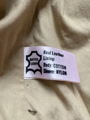 Brun skinnjacka med beige ärmar - Snygg brun skinnjacka med kontrasterande beige ärmar. Jackan har klassisk krage, knäppning framtill och flera fickor. Utsidan är i äkta skinn, fodret i bomull och ärmarna i nylon. Perfekt för dig som vill sticka ut med en unik stil.