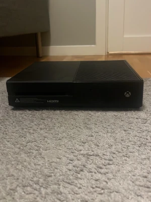 Xbox One spelkonsol svart - Säljer en svart Xbox One spelkonsol från Microsoft. Konsolen har en stilren, rektangulär design med matta och blanka ytor samt ventilerad ovansida. HDMI-port finns på framsidan. Perfekt för gaming och streaming . Kan köpas med en ny kontroll skriv isåfall om du är intresserad!