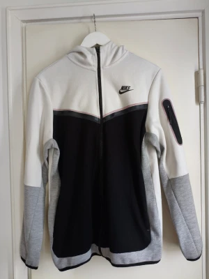 Nike Tech - Nike Tech hoodie i size Large. I bra och fint skick väl omhändertagen. Tillverkad i Tech Fleece-material som ger värme utan att kännas tung. Full zip framtill gör den enkel att använda och styla, och Windrunner-designen ger en modern och sportig look. Passar perfekt till både vardag och streetwear. Nypriset är 1399kr