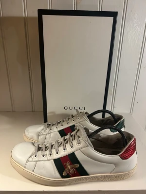 Gucci Ace skor  - Säljer ett par vita Gucci ace bee i stolek 44. Utsidan är i hyfsat bra skick men insidorna är slitna. Av originaltillbehören medkommer box och påsar. OBS: kvitto finns (bild från förra ägaren).