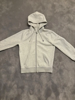 Ljusgrå hoodie från Polo Ralph Lauren - Ljusgrå zip hoodie från polo Ralph lauren. Storlek Smal. Mycket bra skick, inga missfärgningar eller andra skavanker. Nypris ligger på runt 2200