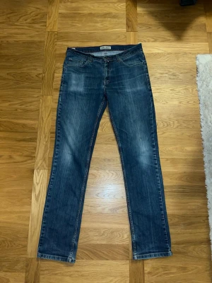 Blå bootcut jeans från Park Lane - Snygga blå jeans från park lane med klassisk bootcut passform. Jeansen har fem fickor, kontrastsömmar och en läderpatch bak i midjan. Tillverkade i slitstarkt denim med subtila slitningar framtill för en cool look. Passar en person som är mellan 175-190 cm 