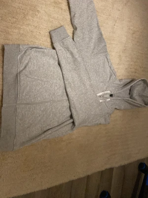 Ljusgrå zip hoodie med huva - Snygg ljusgrå hoodie med dragkedja framtill och två fickor. Klassisk modell med huva och vita dragsnören. Tillverkad i mjukt sweatshirtmaterial som är skönt att ha på sig. Perfekt för en avslappnad stil.