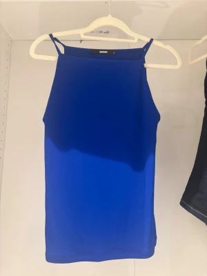 Kornblå linne från Bik Bok - Snyggt kornblått linne från Bik Bok med smala axelband och rak halsringning. Perfekt för sommardagar eller att styla lager på lager. Tillverkad i mjukt och stretchigt material för en bekväm passform.