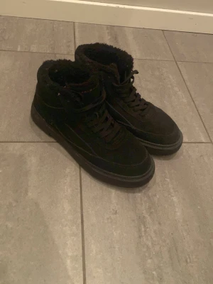 Svarta kängor från Tommy Hilfiger - Snygga svarta kängor från Tommy Hilfiger med mjukt foder och högre skaft. Skorna har snörning framtill och en diskret logga bak på hälen. Utsidan är i mockaliknande material och sulan är robust för extra grepp.