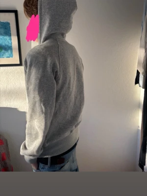 Grå hoodie med broderad logga - Snygg grå hoodie från Burberry med broderad logga på ärmen. Klassisk passform med huva och ribbade muddar vid ärmslut och nederkant. Perfekt för en chill och stilren look. Tillverkad i mjukt bomullsmaterial.