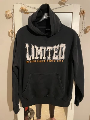 Svart hoodie från Oxide med tryck - Svart hoodie från Oxide med stor vit och orange LIMITED-tryck på bröstet och texten 'Established since 1957'. Klassisk känguruficka framtill och huva. Perfekt för en avslappnad streetwear-look.