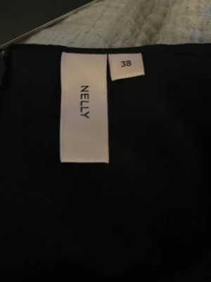 Svart puffärmblus från Nelly - Trendig svart blus från Nelly med korta puffärmar och snygg rynkdetalj längs ryggen. Blusen har en figurnära passform och är tillverkad i ett mjukt tyg som ger en cool och stilren look.