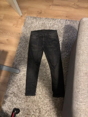 Svarta slim fit jeans från Nudie Jeans - Säljer ett par svarta slim fit jeans från Nudie Jeans. Jeansen har klassisk femficksdesign, svarta sömmar och knappgylf. Materialet är denim i bomull med en lätt tvättad look. Perfekta för en stilren och modern outfit.