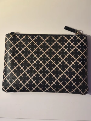 Malene Birger Väska  - Stilren kuvertväska i svart och beige med ett grafiskt rutmönster. Väskan har dragkedja upptill och detaljer i guld. Perfekt att bära till middagen eller när du vill ha med det viktigaste.