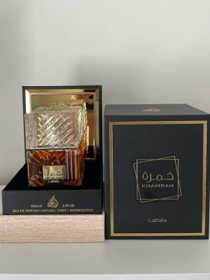 Lattafa Khamrah Eau de Parfum 100ml - Lattafa Khamrah Eau de Parfum kommer i en lyxig svart och guld ask. Flaskan är fyrkantig med ett mönstrat glas i bärnstensfärg och ett transparent lock. Doften är orientalisk och exklusiv, perfekt för dig som vill sticka ut. 