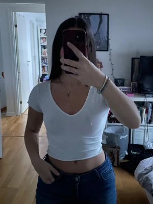 Vit croppad v-ringad topp - Säljer en enkel och stilren vit croppad topp med v-ringning och korta ärmar. Perfekt till jeans eller kjol för en avslappnad look. Materialet känns mjukt och stretchigt, troligtvis bomull eller en bomullsblandning.