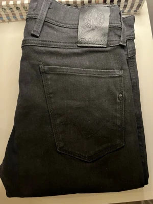 Svarta slim fit jeans från Replay - Snygga svarta slim fit jeans från Replay med klassisk femficksdesign och läderpatch med logga bak i midjan. Jeansen har smal passform och raka ben, perfekta till en trendig streetstyle-look.