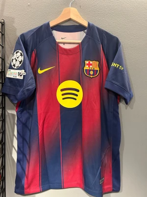 FC Barcelona matchtröja Cubarsí #2 - Säljer en officiell FC Barcelona matchtröja från Nike med Cubarsí #2 på ryggen. Tröjan är röd och blå med gula detaljer, Champions League-märke på ärmen och Spotify-logga på bröstet. Tillverkad i lätt och ventilerande material, perfekt för fotbollsträning eller match. Helt ny med tagg. En replika