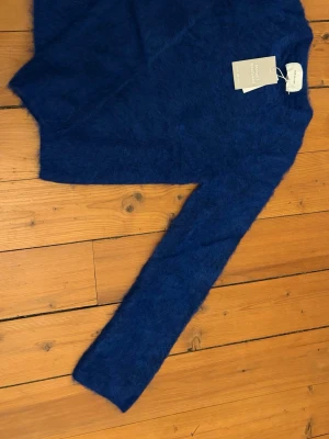 Blå fluffig mohairtröja H&M Edition - Mysig blå stickad tröja från H&M Edition i en fluffig mohair- och ullblandning. Tröjan har lång ärm och enkel, klassisk rund halsringning. Perfekt för dig som gillar en trendig och bekväm look.