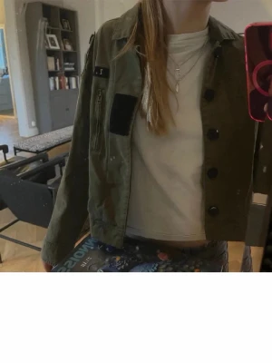 Grön overshirt från Zadig & Voltaire - Snygg militärgrön overshirt från Zadig & Voltaire med svarta knappar och cool patchdetalj på bröstet. Jackan har en dragkedjeficka och klassisk krage, perfekt att slänga över en t-shirt. Stilsäker och enkel att matcha med jeans eller kjol. Storlek xs!💖 jätte fin vår jacka