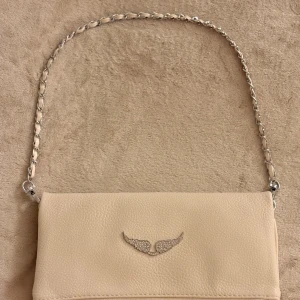 Beige kuvertväska med kedjerem - Stilren beige Zaldig & Voltaire väska i skinn. Fått i födelsedagspresent men inte riktigt min typ av väska så säljer istället. Jättefint skick och inte använd mycket alls. 