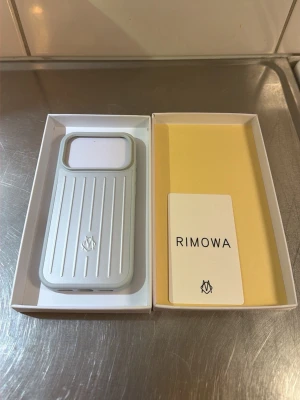 Rimowa mobilskal i ljusgrått - Snyggt mobilskal från Rimowa i ljusgrå färg med klassiska räfflade linjer och logga på baksidan. Skalets material känns robust och exklusivt, perfekt för dig som vill ha en stilren look till mobilen. Kommer i originalförpackning.