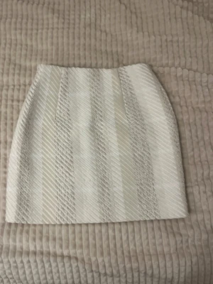 Beige kortkjol från H&M i XS - Säljer en beige kortkjol från H&M i storlek XS. Kjolen har ett snyggt randigt mönster med struktur och är gjord i ett tjockare material som känns lyxigt.