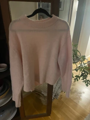 Ljusrosa stickad tröja Gina Tricot - Mysig ljusrosa stickad tröja från Gina Tricot med rund halsringning och ribbade muddar vid ärmslut och nederkant. Tröjan har en avslappnad passform och är perfekt för att hålla värmen under kyliga dagar.