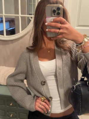 Grå ribbstickad kofta med stora knappar - Säljer en croppad grå ribbstickad kofta med tre stora knappar framtill. Koftan har en avslappnad passform och långa ärmar, perfekt att slänga över ett linne eller t-shirt. Enkel och stilren design som passar till det mesta. Koftan är i ett bra skick och köpt från HM, tror dock inte den säljs längre. Vill sälja den eftersom att jag personligen inte tycker att jag passar i grått.