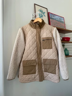 Quiltad jacka med teddy  - Supersnygg och praktisk jacka i beige/ljusbruna toner med quiltad kropp och mjuka teddyfleece-ärmar. Passande för både vår, höst och mild vinter! ✨Se även mina andra annonser, 3 för 2 på allt! ✨ 