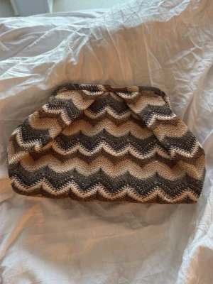 Beige och brun kuvertväska med zigzag - Kuvertväska från becksöndergaard i beige och bruna toner med ett snyggt zigzag / missoni mönster. Den är i jättefint skick men har några enstaka trådar som sticker ut, inget man tänker på däremot. 