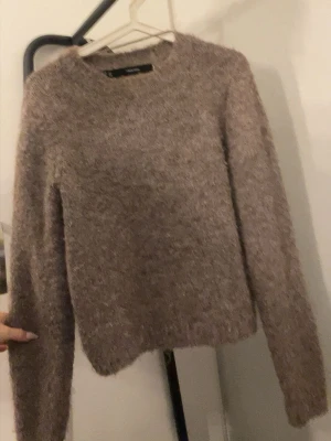 Beige fluffig stickad tröja - Mysig beige stickad tröja från Knit med fluffig känsla. Tröjan har rund halsringning och långa ärmar, perfekt för lager-på-lager. Materialet är mjukt och ger en avslappnad vibe.