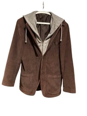 Brun kavaj med grå huva - Snygg brun kavaj i manchester med grå huva och dragsko. Två stora fickor framtill och cool detalj med tryck på huvan. Perfekt för dig som vill ha en avslappnad men ändå stilren look.