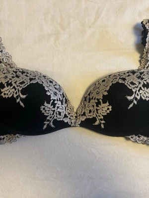 Svart push-up bh med spetsdetaljer - Superfin bh med blommig spets köpt på plick! Säljer då den tyvärr inte passar mig