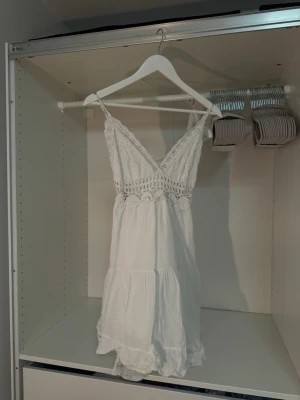 Vit spetsklänning med smala axelband - Söt vit kortklänning med smala axelband och v-ringning. Överdelen har fina spetsdetaljer och virkad kant, samt ett genombrutet parti under bysten. Öppen rygg med knyten och kjolen faller fint. Kjolen är lätt och luftig med volang. Perfekt för sommarens varma dagar. Drömmig utomlandsklänning😍🥹 Står ej storlek men köpt på spansk marknad och skulle uppskatta XS-S